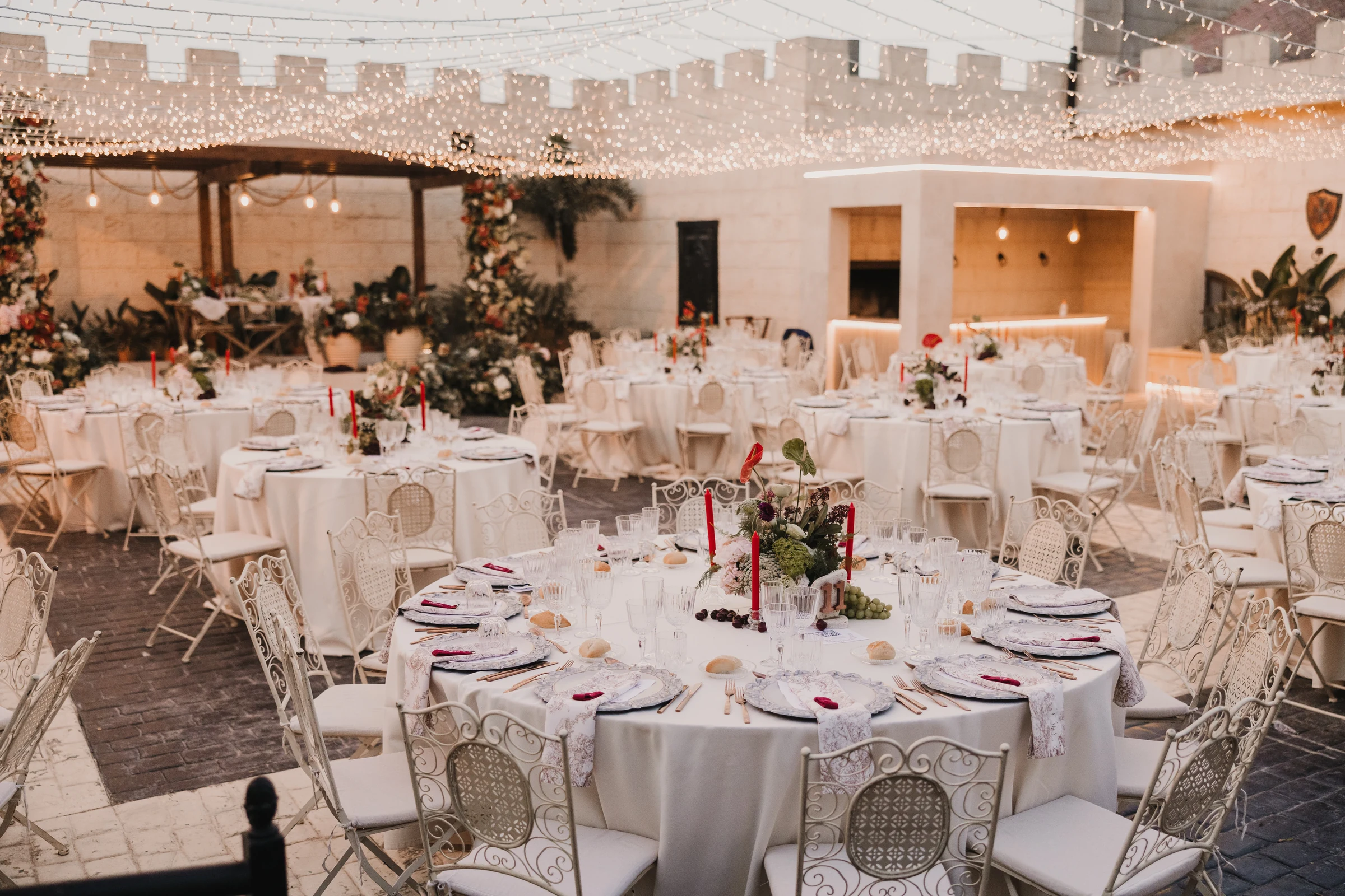 Mesas del banquete con flores, mantelería y cristalería bajo las guirnaldas del patio